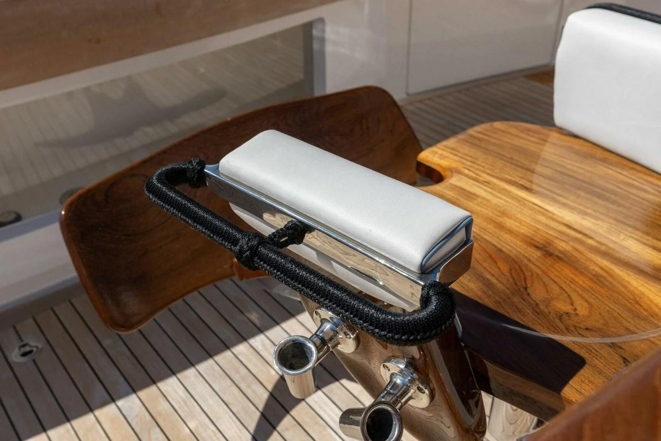 A close-up of a polished wooden yacht detail with stainless steel fittings and a cushioned armrest. aboard TEAM HARVEY I Yacht for Sale