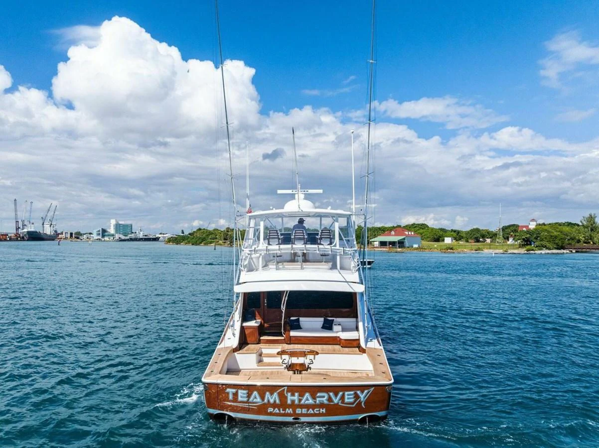 A yacht is seen from the rear, cruising on calm waters under a bright blue sky. aboard TEAM HARVEY I Yacht for Sale