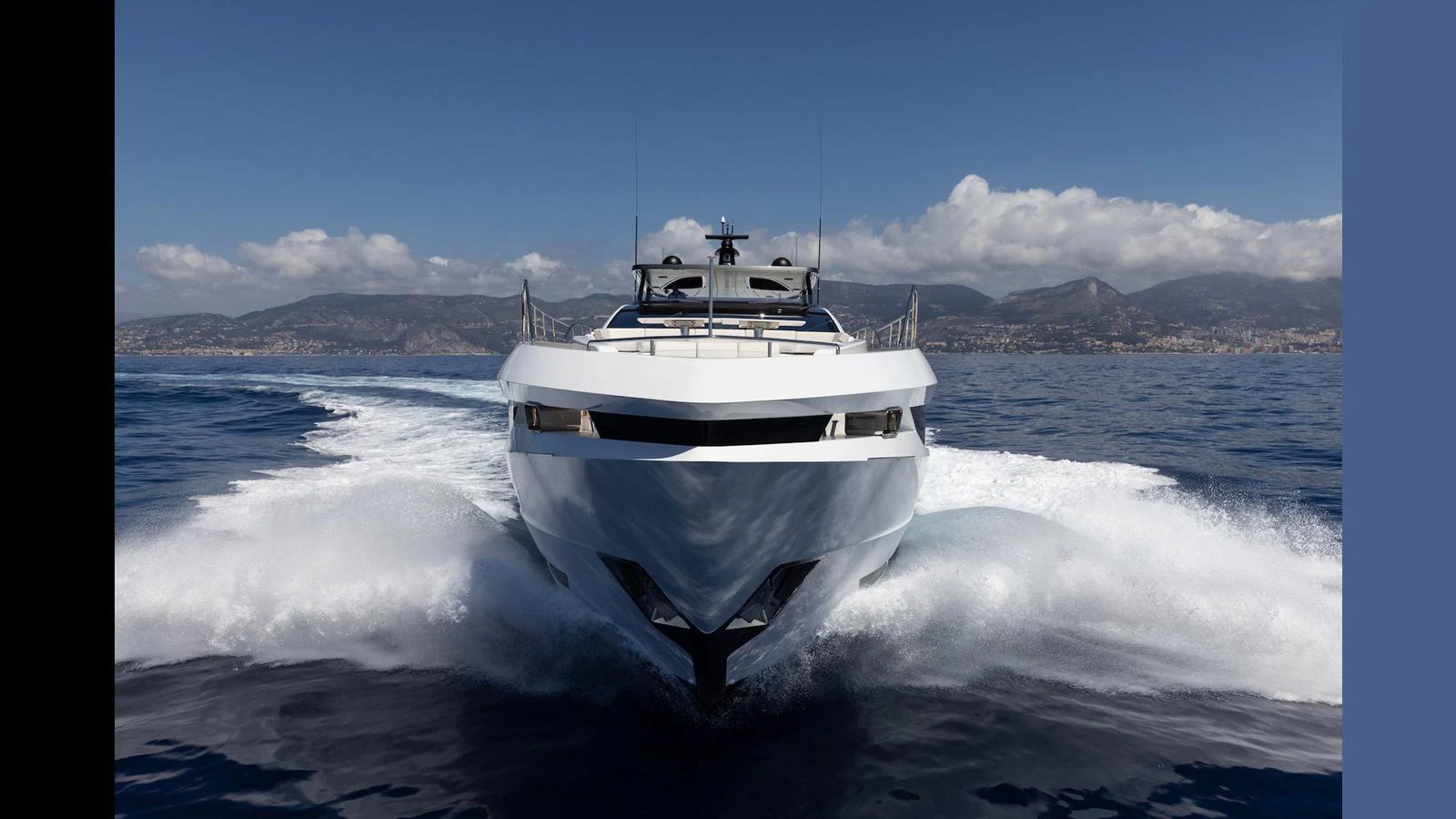 A sleek yacht cuts through the water, showcasing its modern design against a backdrop of mountains and clear skies. aboard ARTEMIS Yacht for Sale