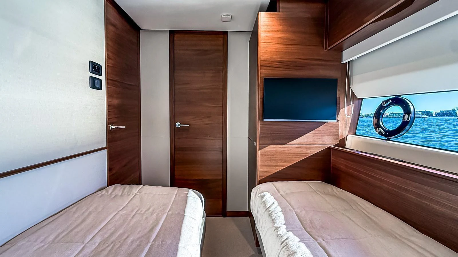 The guest stateroom features twin beds, a flat-screen TV, and a view of the water through a porthole window. aboard NAUTILUS Yacht for Sale