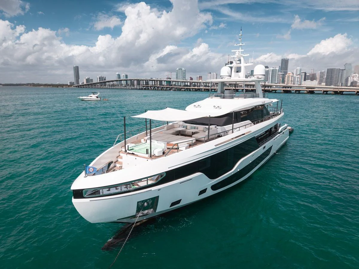 A sleek and modern yacht cruising in clear blue waters with a city skyline in the background. aboard TYCOON Yacht for Sale