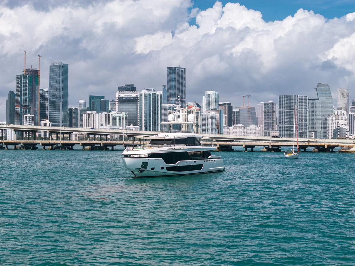 A sleek yacht cruises in front of a vibrant city skyline, showcasing its modern design. aboard TYCOON Yacht for Sale