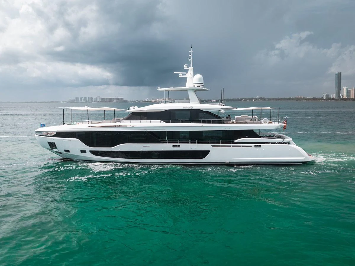 A sleek and modern yacht cruises through turquoise waters under a cloudy sky. aboard TYCOON Yacht for Sale