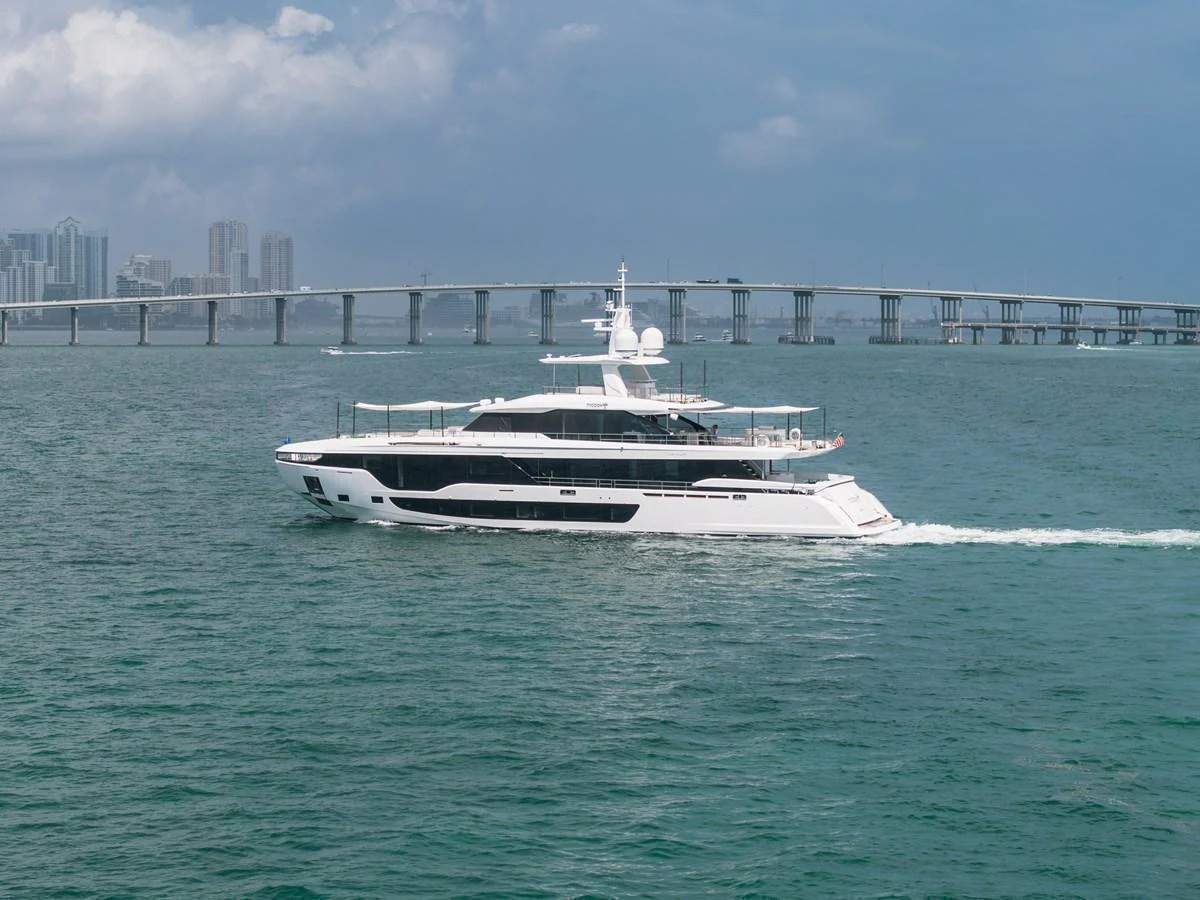 A sleek and modern yacht cruises through calm waters with a cityscape and bridge in the background. aboard TYCOON Yacht for Sale