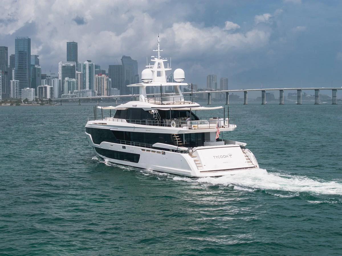 A luxurious yacht cruises through the water with a city skyline in the background. aboard TYCOON Yacht for Sale