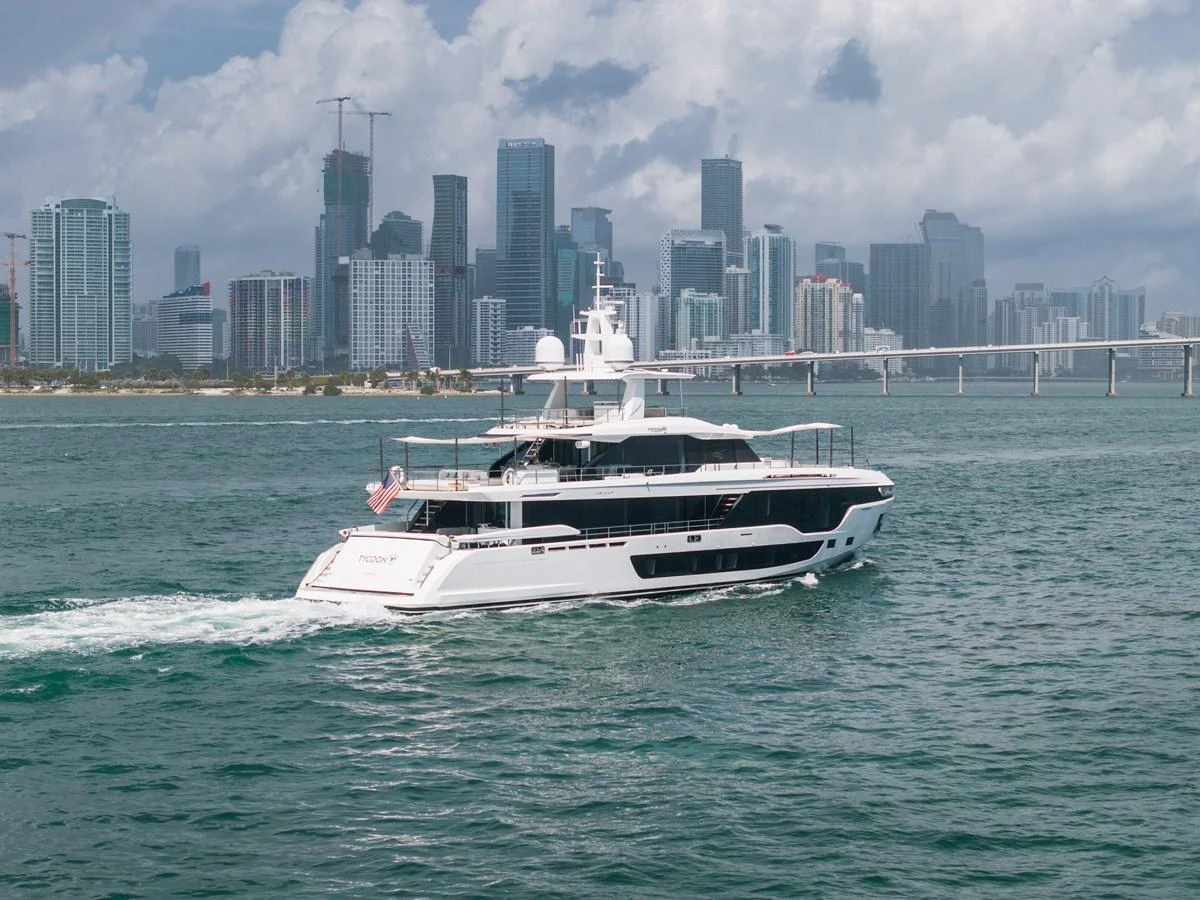 A sleek yacht cruises through the water with a city skyline in the background. aboard TYCOON Yacht for Sale