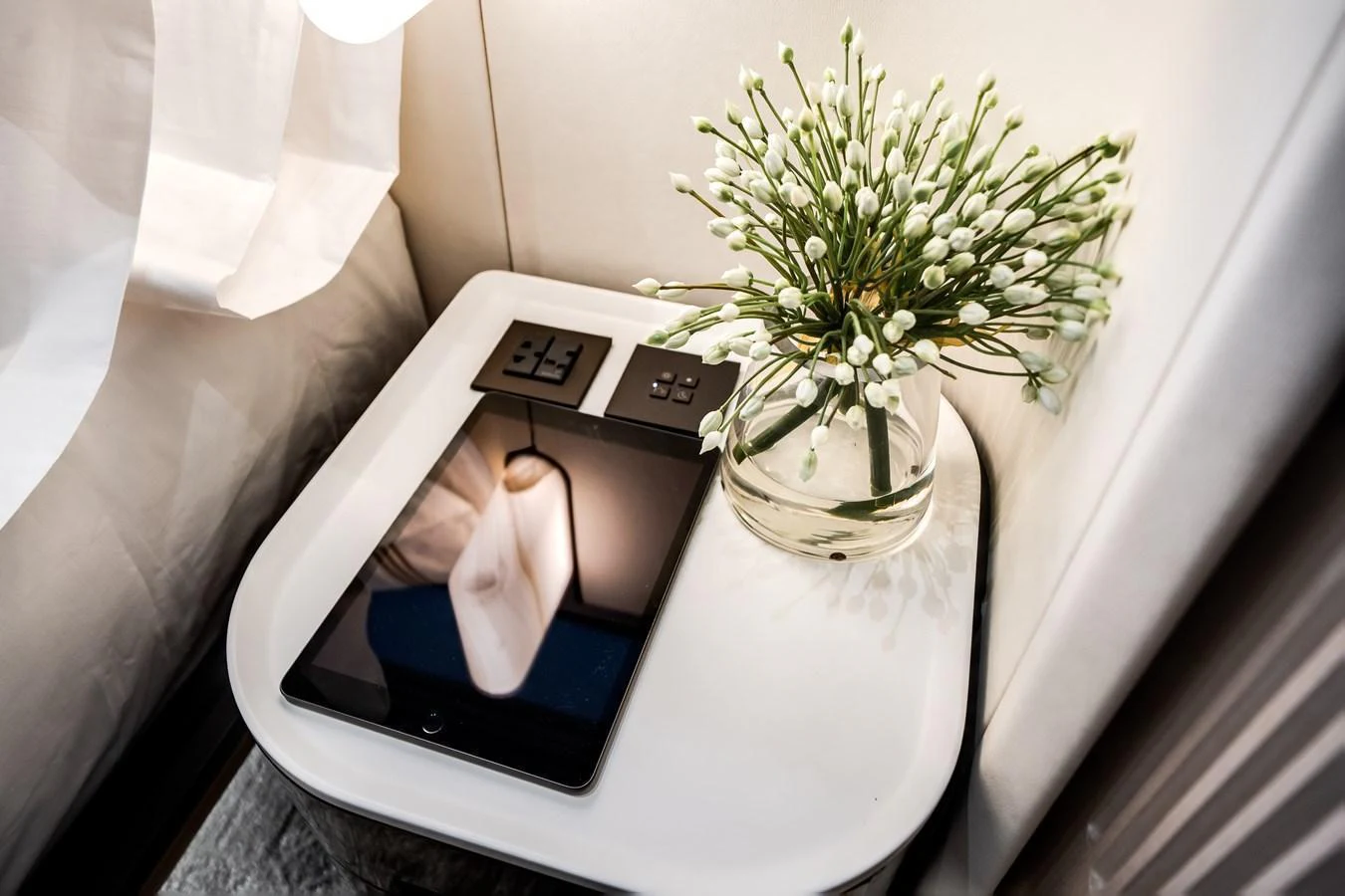 A close-up of a stylish bedside table with a tablet and a vase of flowers. aboard TYCOON Yacht for Sale