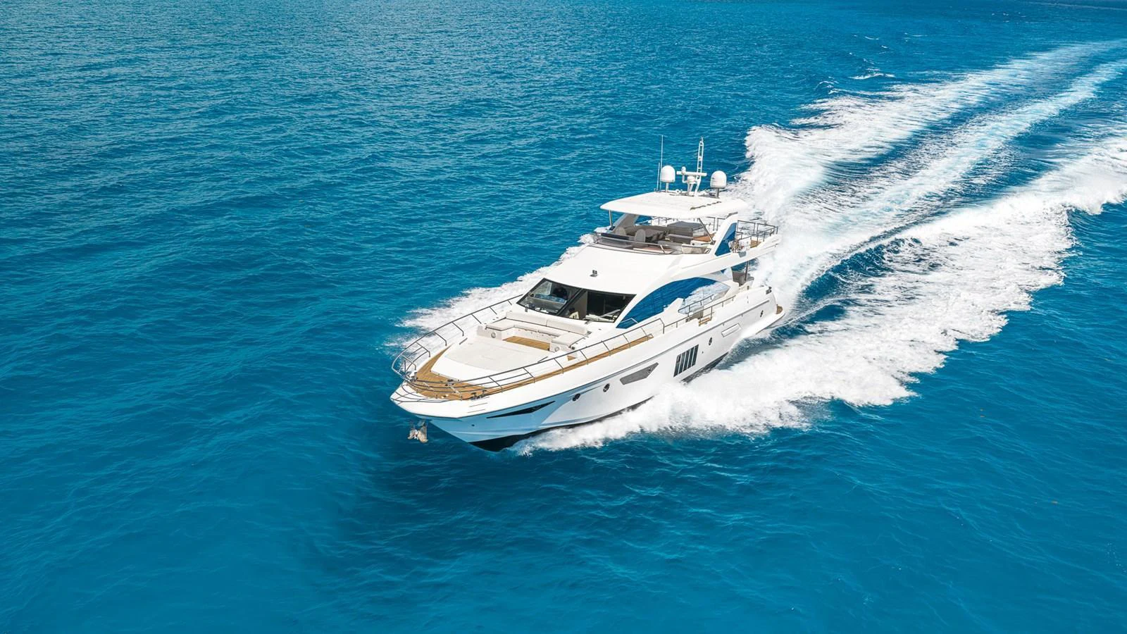 A sleek yacht cruises swiftly through vibrant blue waters, leaving a trail of white wake behind. aboard SABI Yacht for Sale