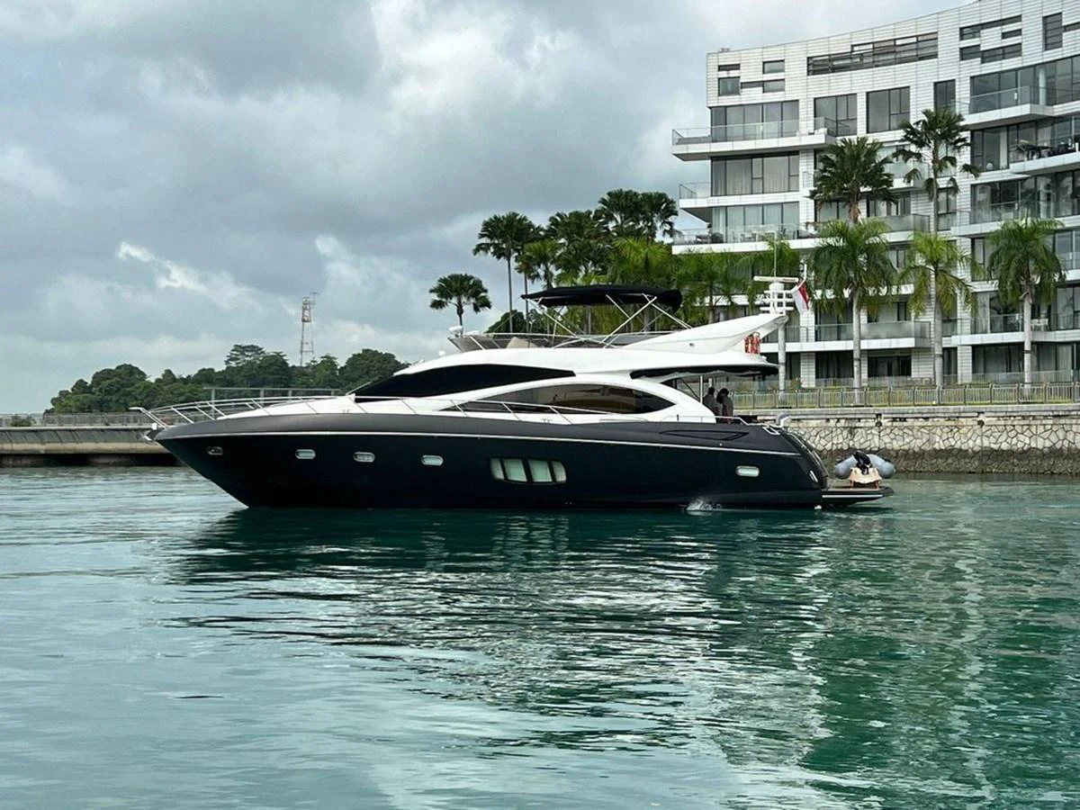 A sleek and modern yacht is docked near a contemporary waterfront building, showcasing its elegant lines and spacious design. aboard ELLYN Yacht for Sale