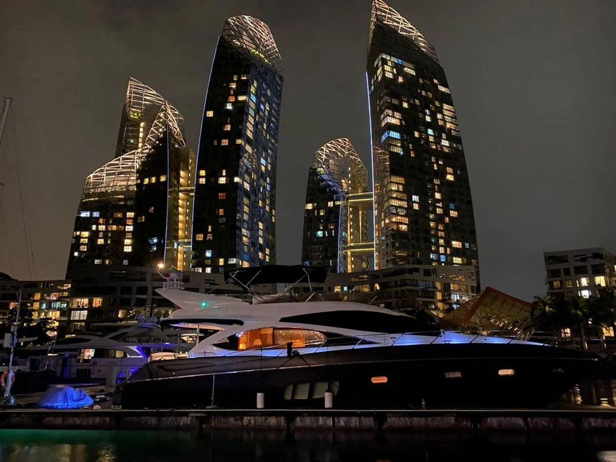 A sleek yacht is docked at night against a backdrop of illuminated modern skyscrapers. aboard ELLYN Yacht for Sale