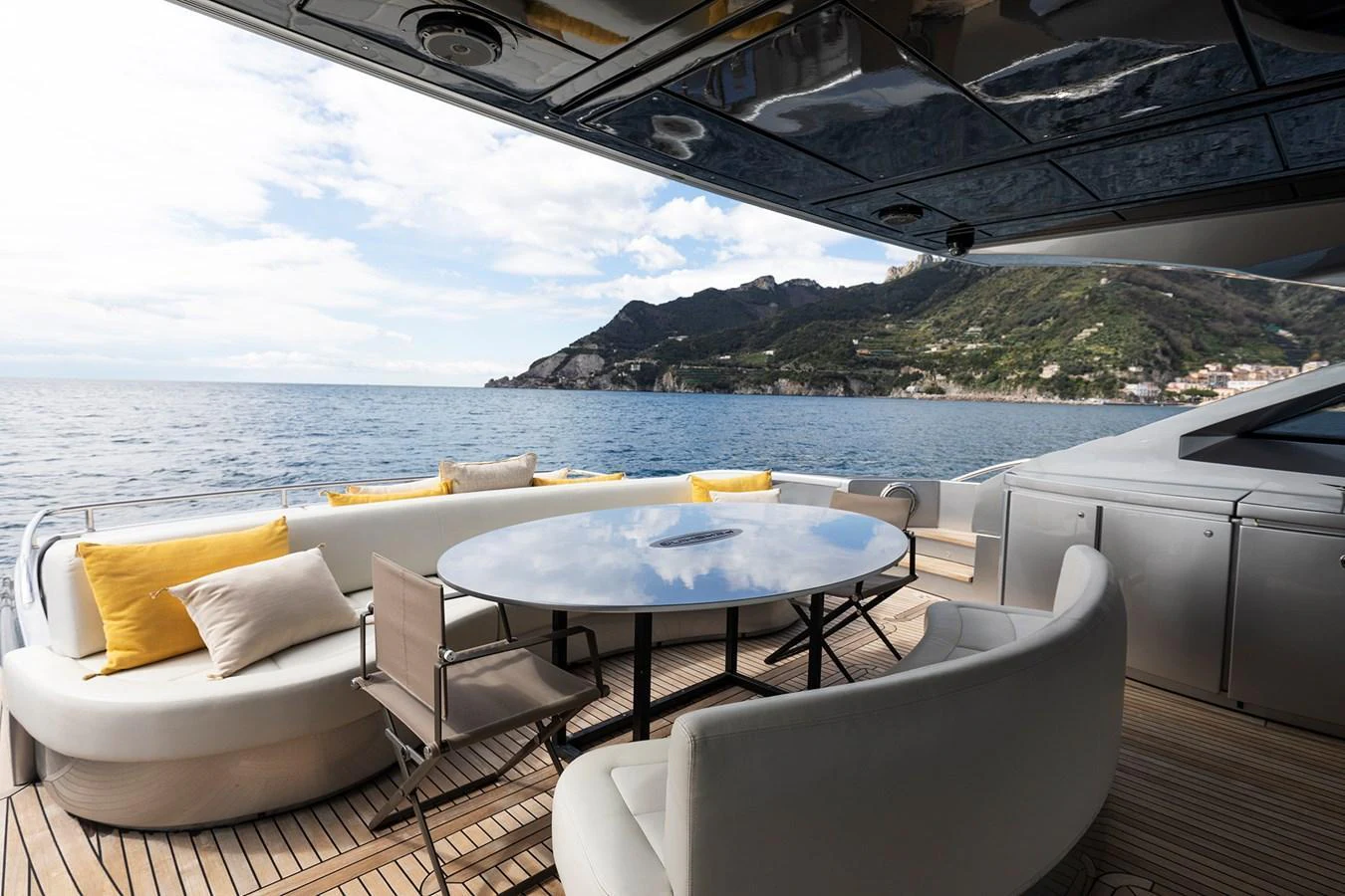 The aft deck features a stylish outdoor dining area with a round table and comfortable seating, offering stunning views of the surrounding waters and coastline. aboard GRACE Yacht for Sale