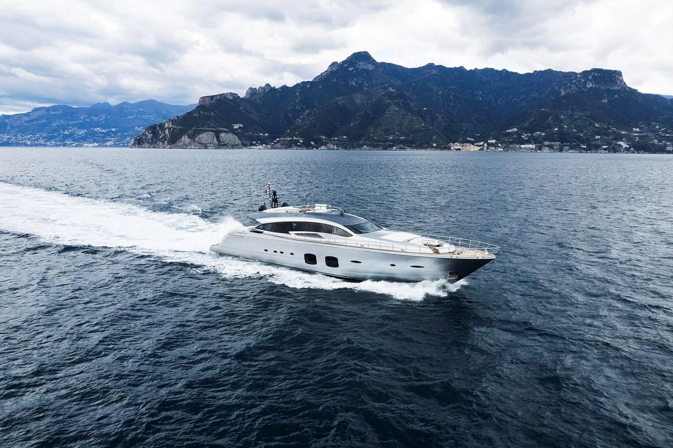 A sleek yacht cruises through open waters with a mountainous coastline in the background. aboard GRACE Yacht for Sale