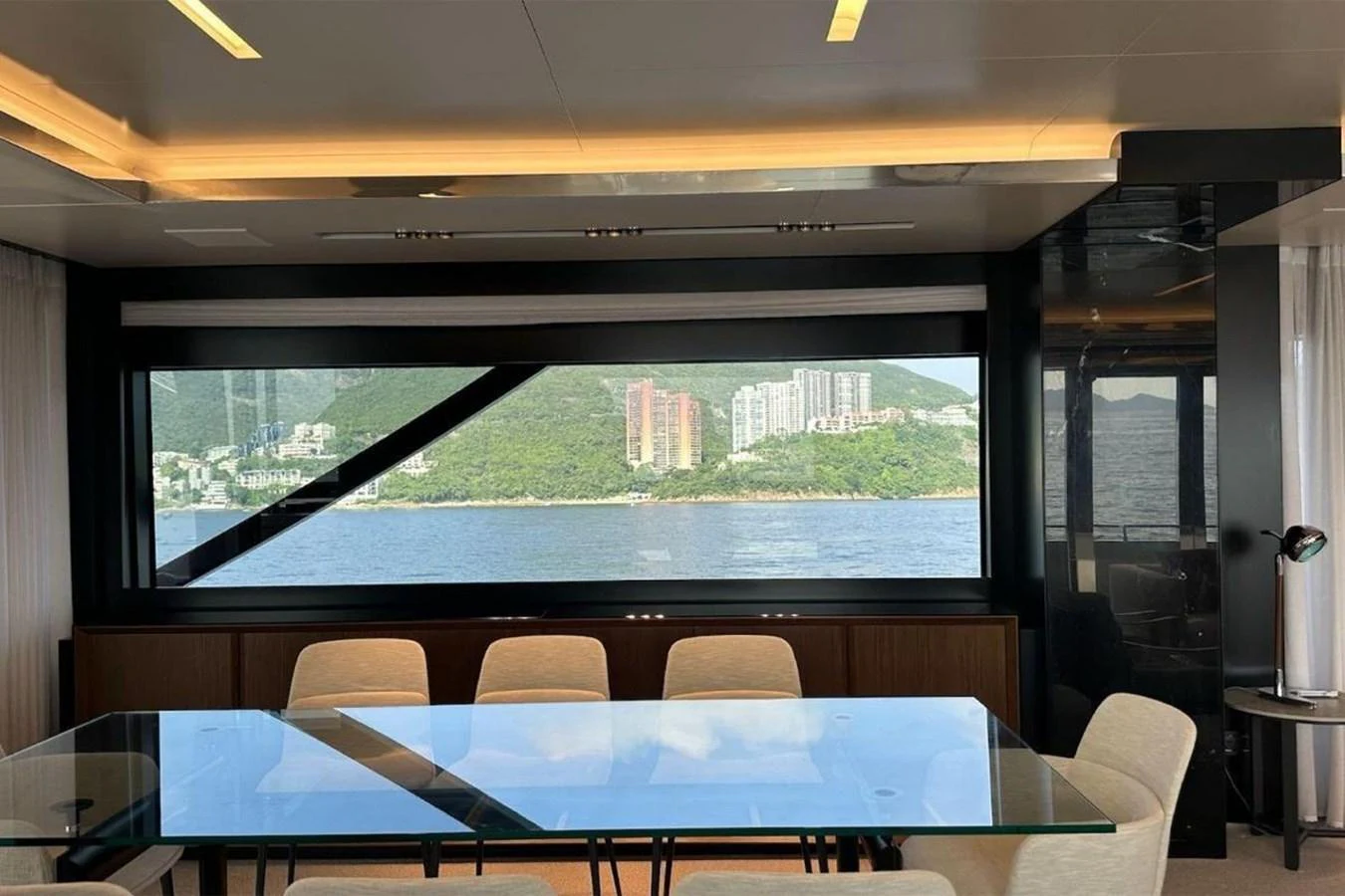 The yacht's dining area features a sleek glass table with a stunning view of the coastline through large windows. aboard BELLA DONNA Yacht for Sale