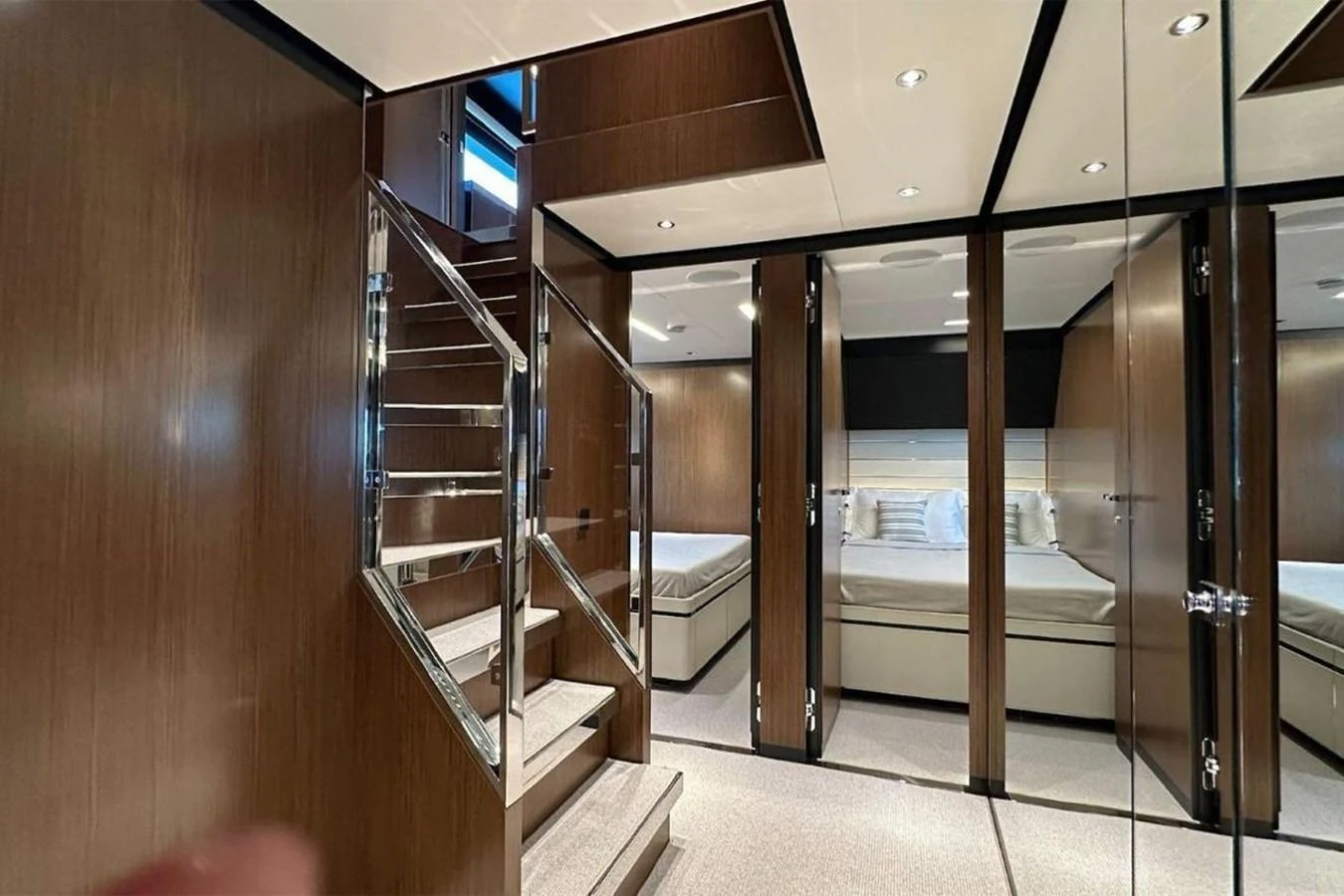 The image showcases a luxurious stateroom with elegant wooden finishes and a mirrored wall, leading to a cozy sleeping area. aboard BELLA DONNA Yacht for Sale