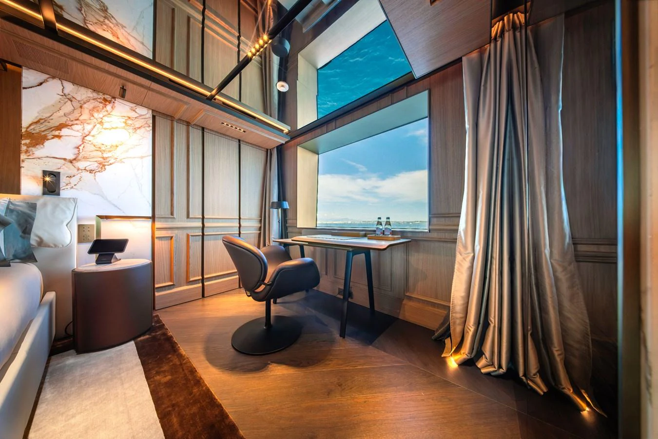 A luxurious stateroom featuring elegant wood paneling, a comfortable desk area, and a large window with a stunning sea view. aboard RAJA Yacht for Sale