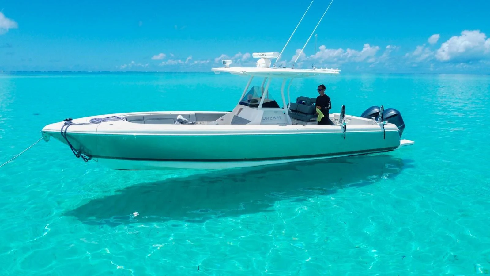 A sleek yacht glides effortlessly over crystal-clear turquoise waters under a bright blue sky. aboard DREAM Yacht for Sale