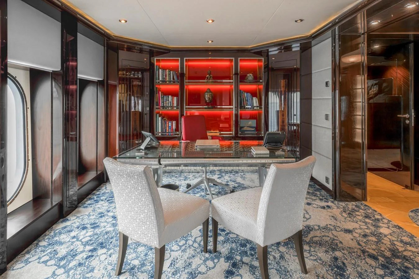 The yacht's office features a sophisticated design with a large desk, comfortable chairs, and a striking red-lit bookshelf. aboard DREAM Yacht for Sale