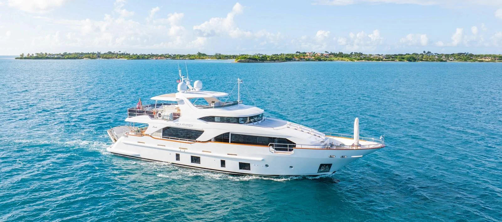 A luxurious yacht cruises through serene blue waters under a clear sky. aboard SEA GYPSY Yacht for Sale