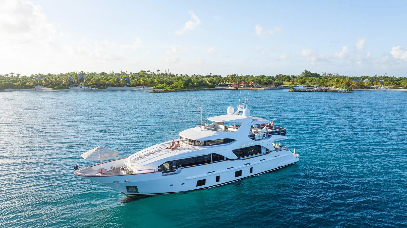 A luxurious yacht cruises serenely in clear blue waters near a lush, tropical shoreline. aboard SEA GYPSY Yacht for Sale