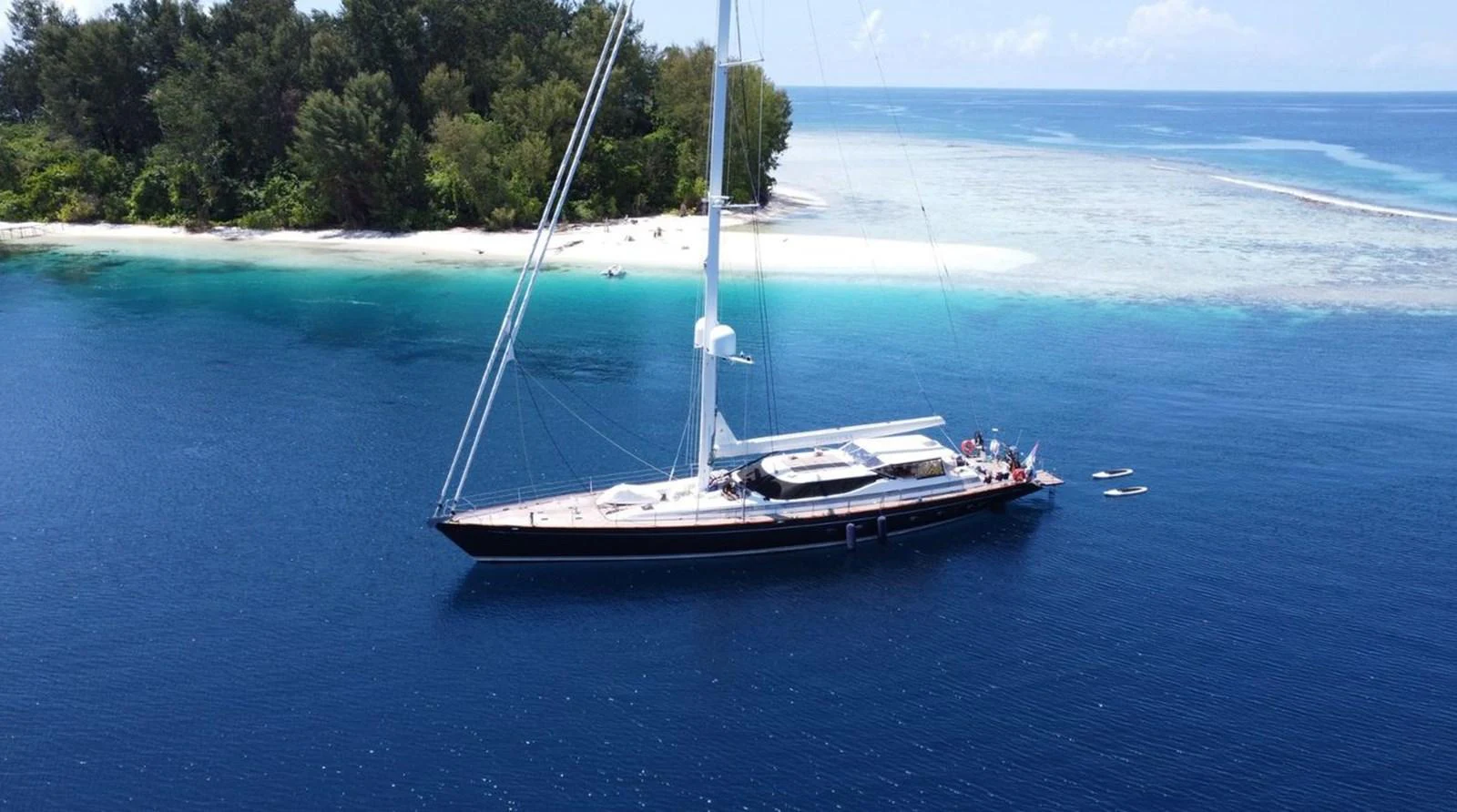 A sleek sailing yacht is anchored in a serene tropical bay with crystal-clear waters and lush greenery in the background. aboard THANDEKA Yacht for Sale
