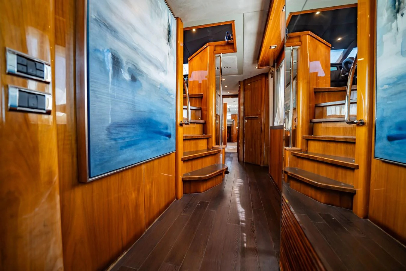 The yacht's interior features a polished wooden staircase with modern artwork adorning the walls. aboard BLUE Yacht for Sale