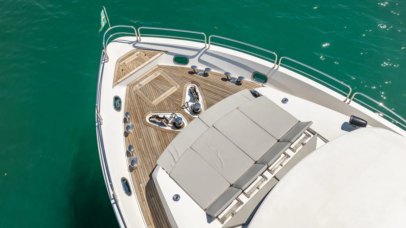 The foredeck features a spacious sunbathing area with plush cushions and teak decking, surrounded by clear blue waters. aboard BLUE Yacht for Sale