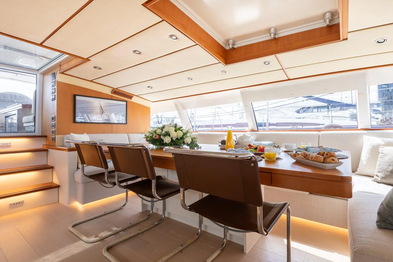 The yacht's dining area is elegantly set with a table adorned with flowers and breakfast items, surrounded by comfortable seating and ample natural light. aboard 4K Yacht for Sale