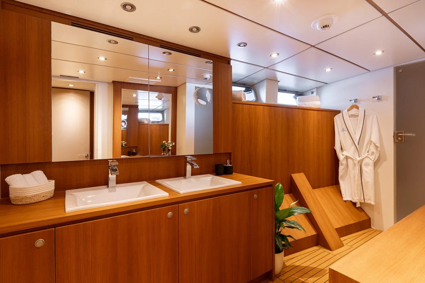 A luxurious yacht bathroom featuring dual sinks, wooden cabinetry, and a plush robe. aboard 4K Yacht for Sale