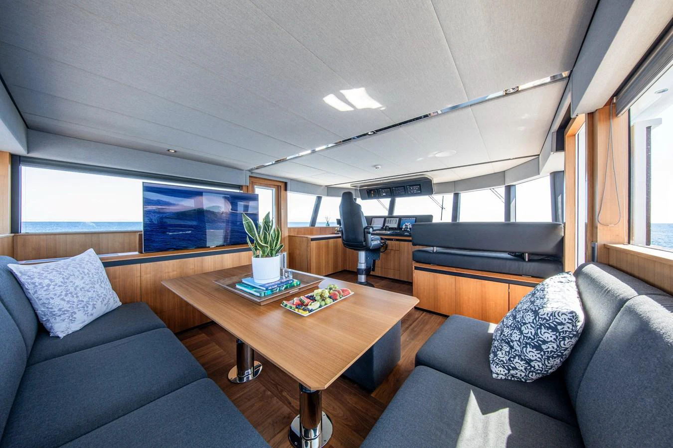 The salon features a spacious seating area with a central table, large windows, and modern decor. aboard PLAYA Yacht for Sale