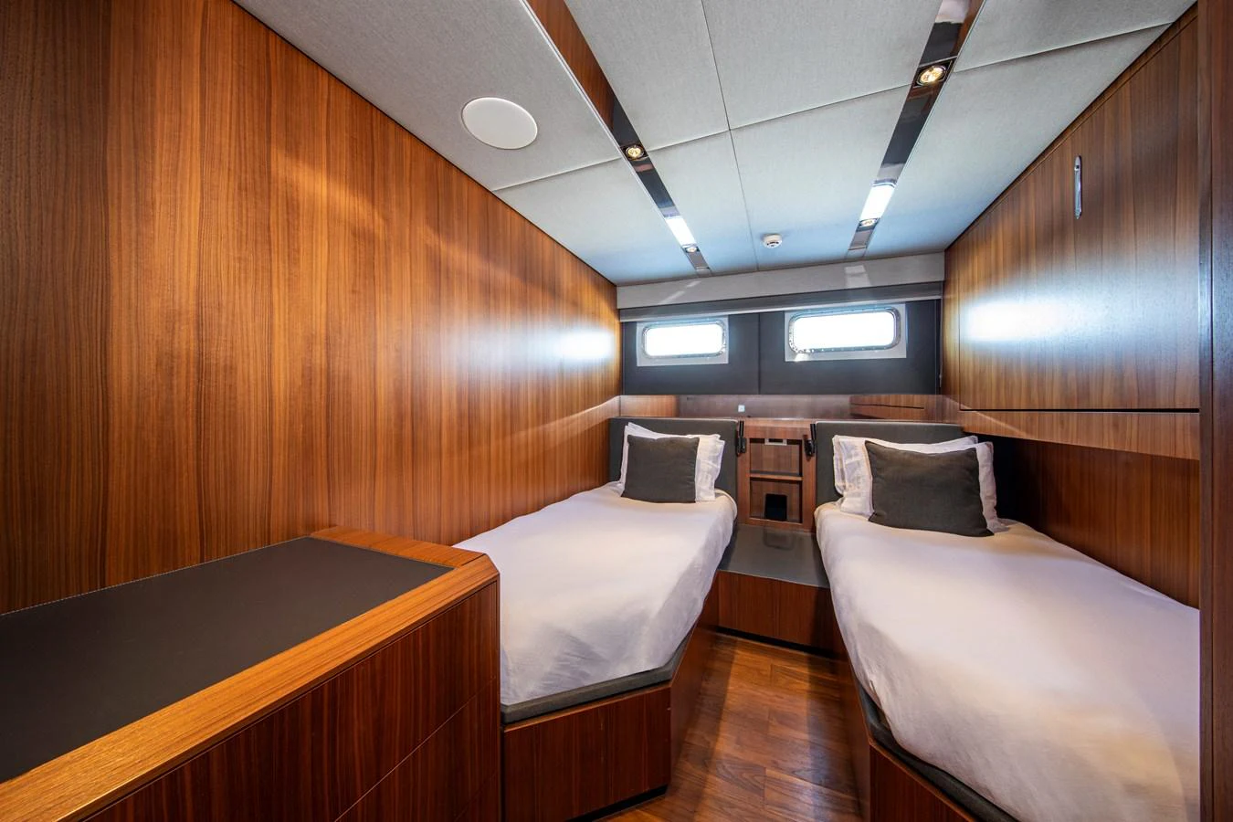 The guest stateroom features twin beds with sleek wooden paneling and modern lighting. aboard PLAYA Yacht for Sale