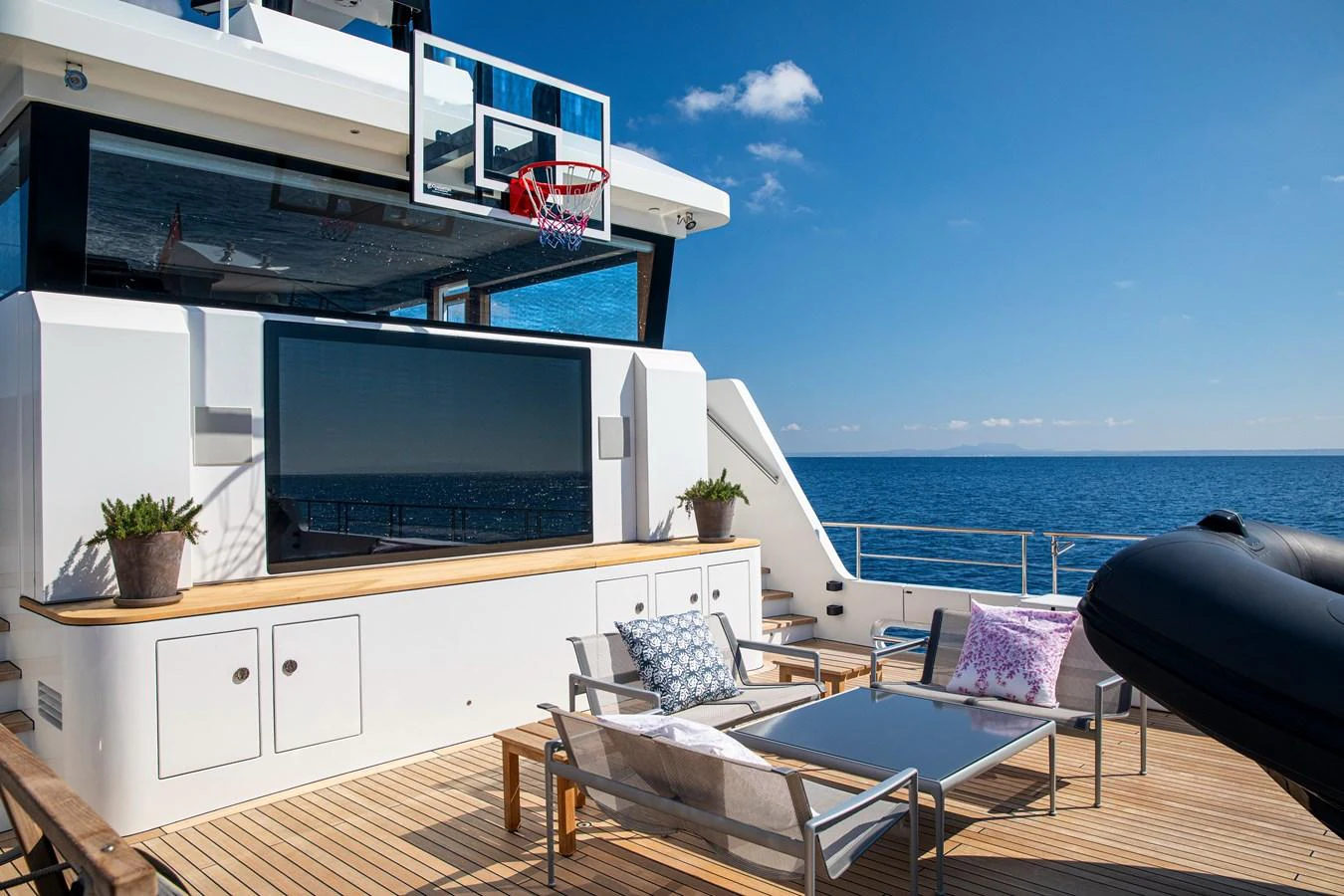 The aft deck features a basketball hoop, a large TV, and comfortable seating with ocean views. aboard PLAYA Yacht for Sale