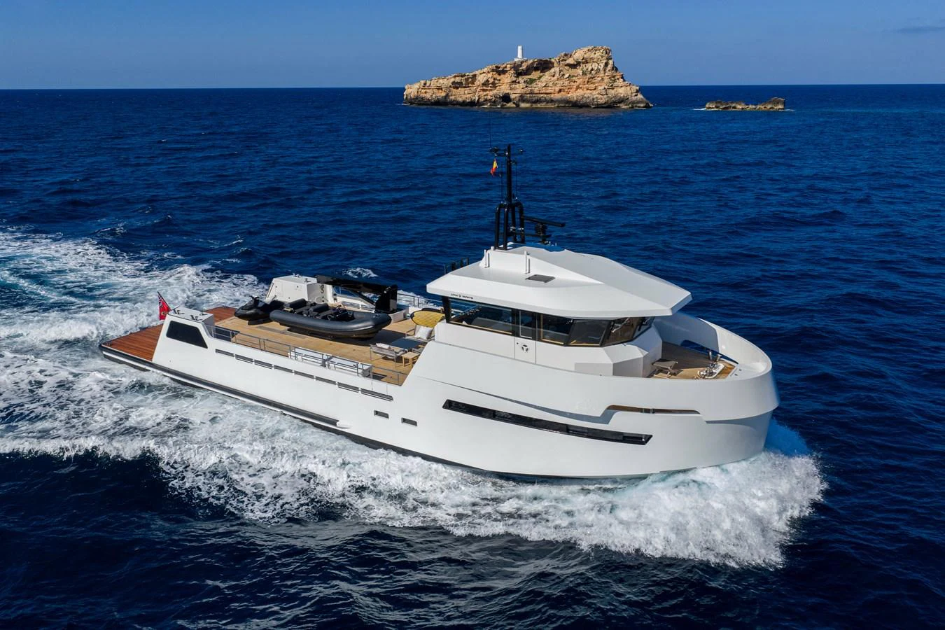 A sleek, modern yacht cruises through the deep blue sea with an island in the background. aboard PLAYA Yacht for Sale