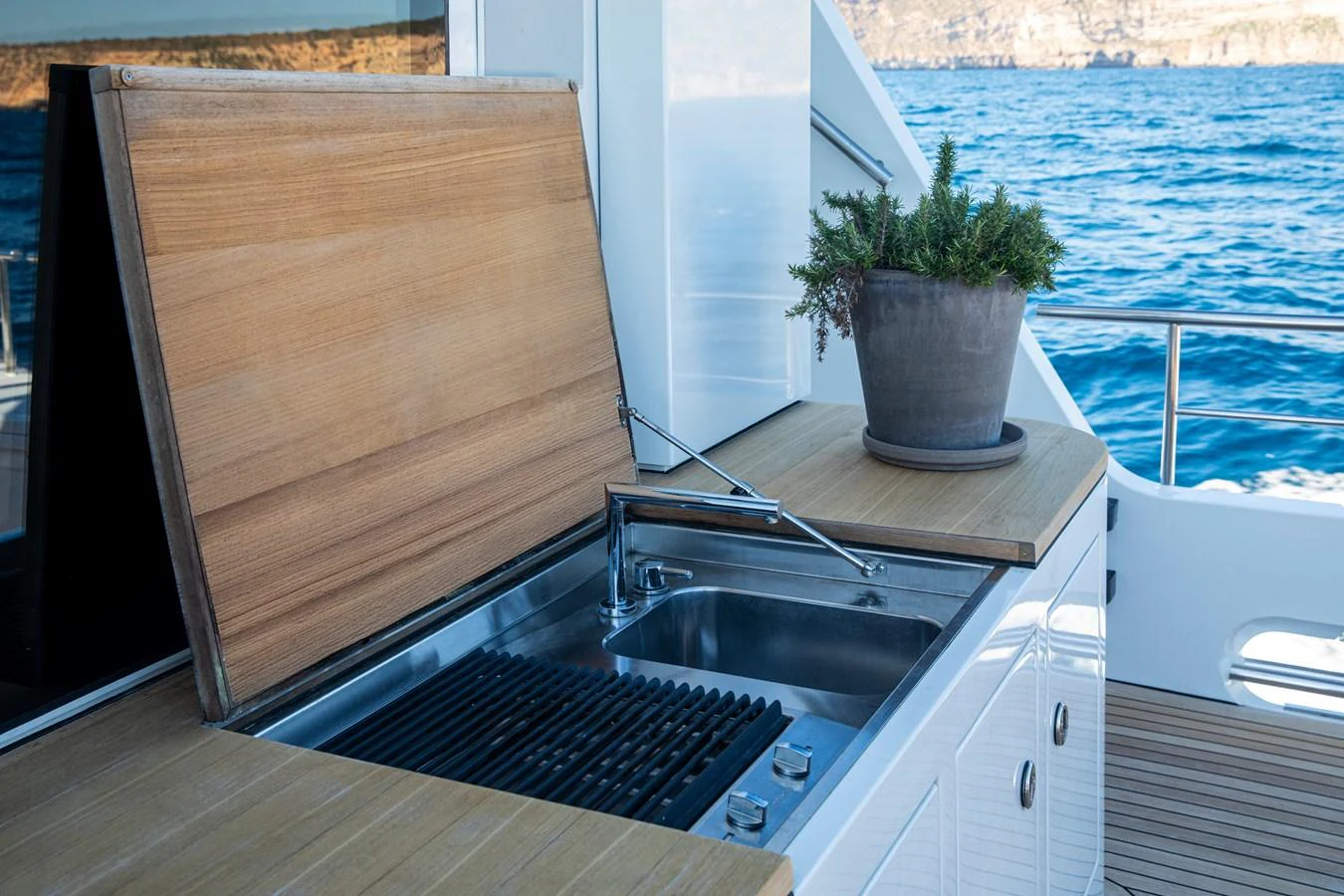 An outdoor galley with a grill and sink, complemented by a potted plant, offers a convenient cooking space with a scenic ocean view. aboard PLAYA Yacht for Sale