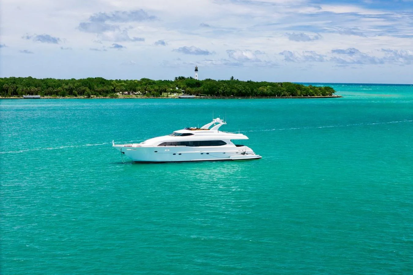 A sleek white yacht cruises through turquoise waters with a lush island in the background. aboard TRANQUILITY IV - 94 FT LAZZARA MOTORYACHT 2001 Yacht for Sale