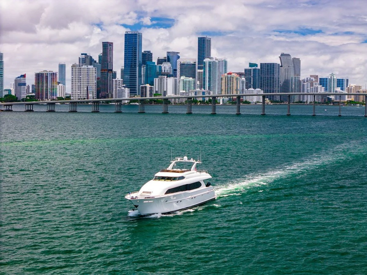 A sleek yacht cruises through vibrant green waters with a stunning city skyline in the background. aboard TRANQUILITY IV - 94 FT LAZZARA MOTORYACHT 2001 Yacht for Sale