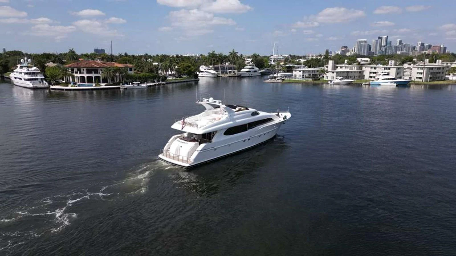 A sleek white yacht cruises through a calm marina with a cityscape in the background. aboard TRANQUILITY IV - 94 FT LAZZARA MOTORYACHT 2001 Yacht for Sale