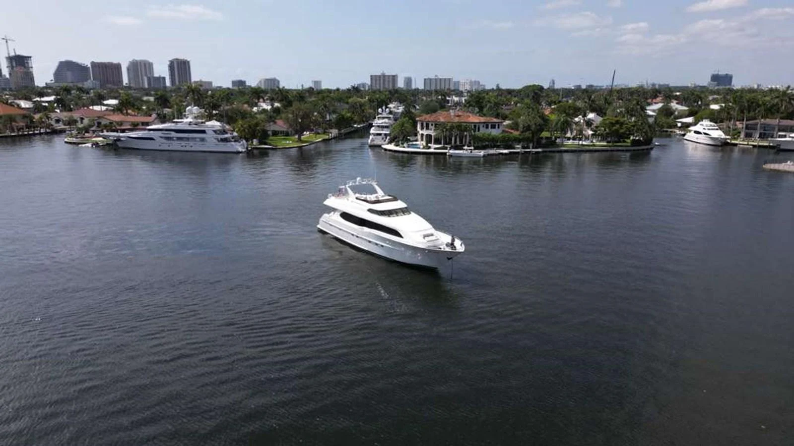 A sleek yacht cruises through a serene waterfront area with other boats and buildings in the background. aboard TRANQUILITY IV - 94 FT LAZZARA MOTORYACHT 2001 Yacht for Sale
