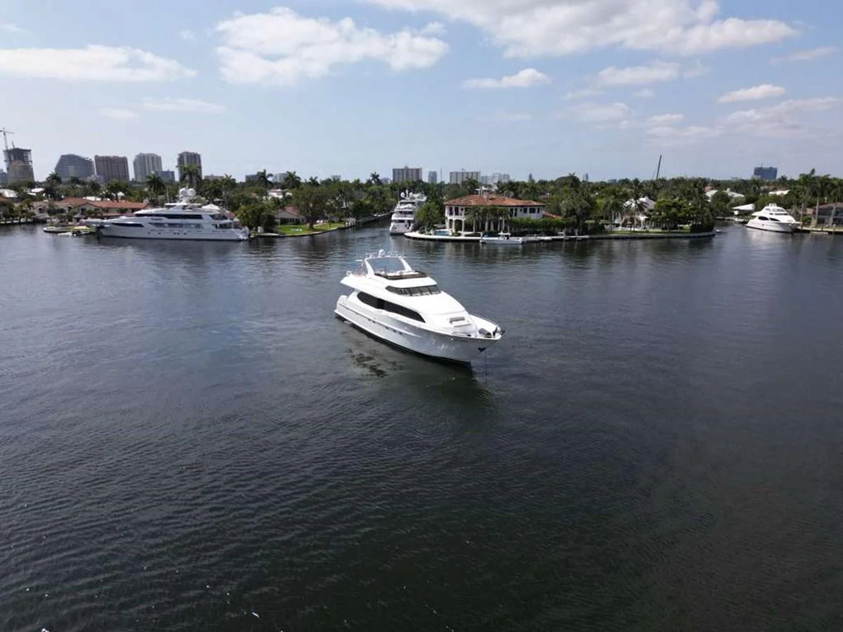 A sleek white yacht cruises through a serene waterfront with a backdrop of luxurious homes and other yachts. aboard TRANQUILITY IV - 94 FT LAZZARA MOTORYACHT 2001 Yacht for Sale