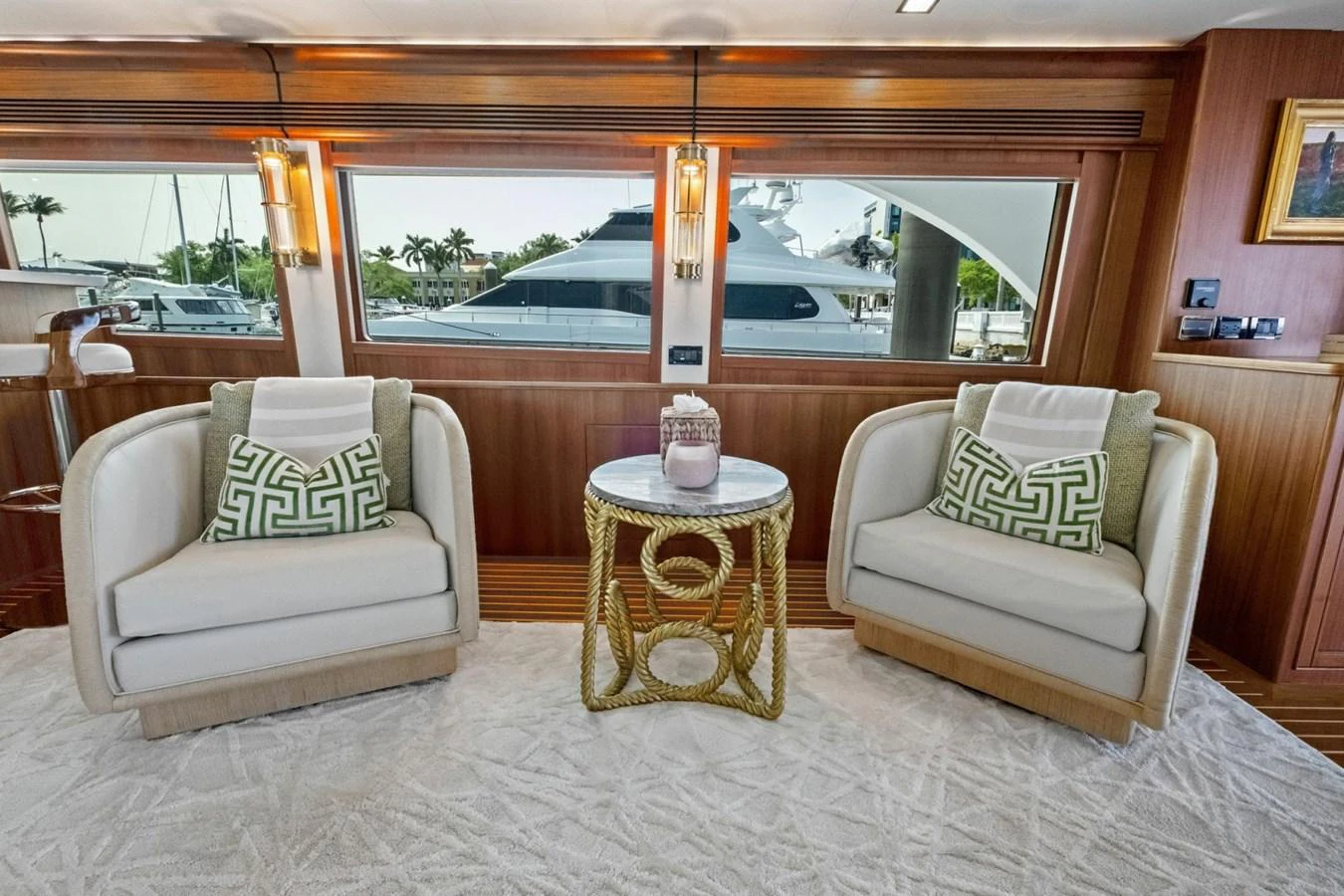 The yacht's interior features a cozy seating area with two armchairs and a small round table, complemented by large windows offering a view of the marina. aboard ARTEMIS II Yacht for Sale