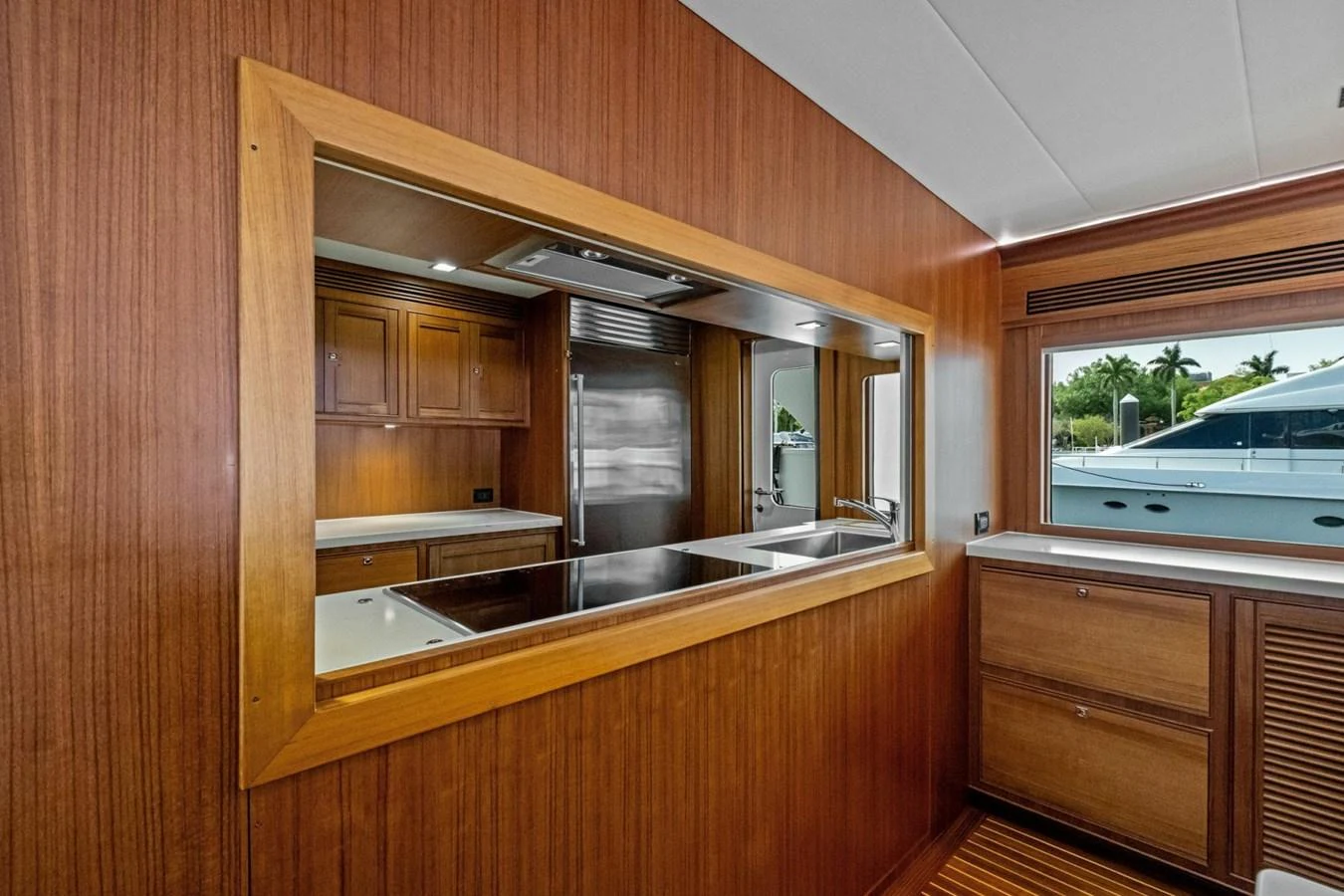 The galley features rich wooden cabinetry and modern stainless steel appliances, with a view of the exterior through a large window. aboard ARTEMIS II Yacht for Sale