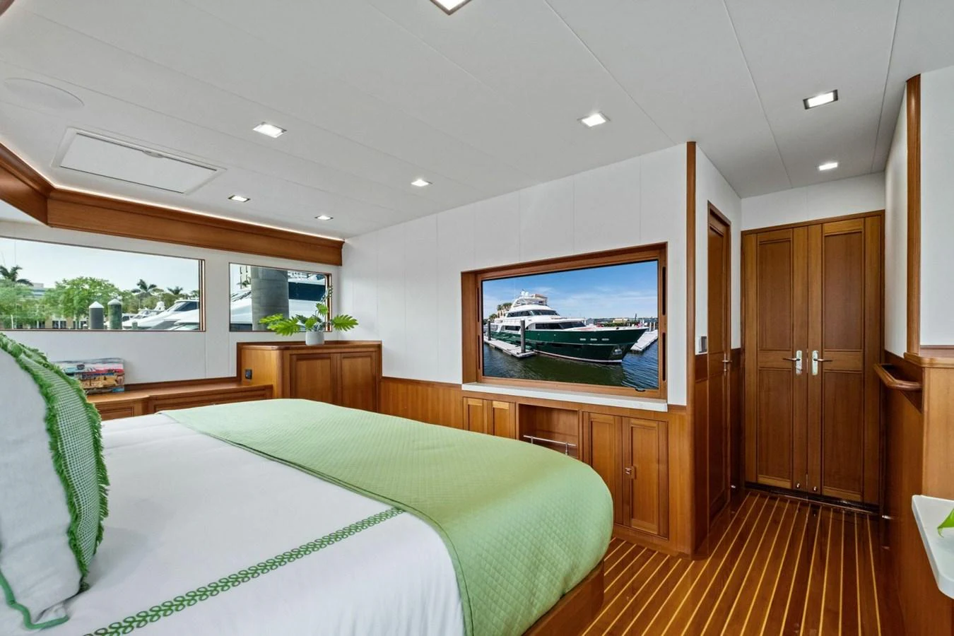 A luxurious stateroom featuring a comfortable bed with green accents and a large window providing a view of the marina. aboard ARTEMIS II Yacht for Sale
