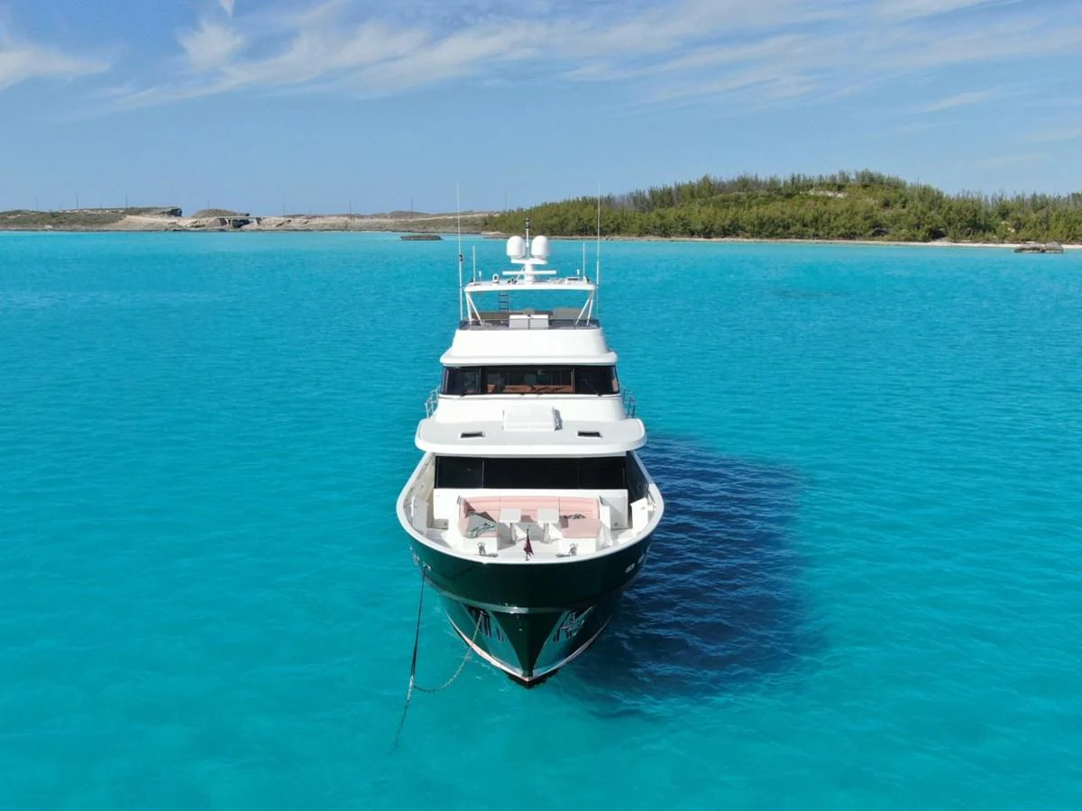 A luxurious yacht is anchored in crystal-clear turquoise waters with a scenic backdrop of lush greenery and blue skies. aboard ARTEMIS II Yacht for Sale