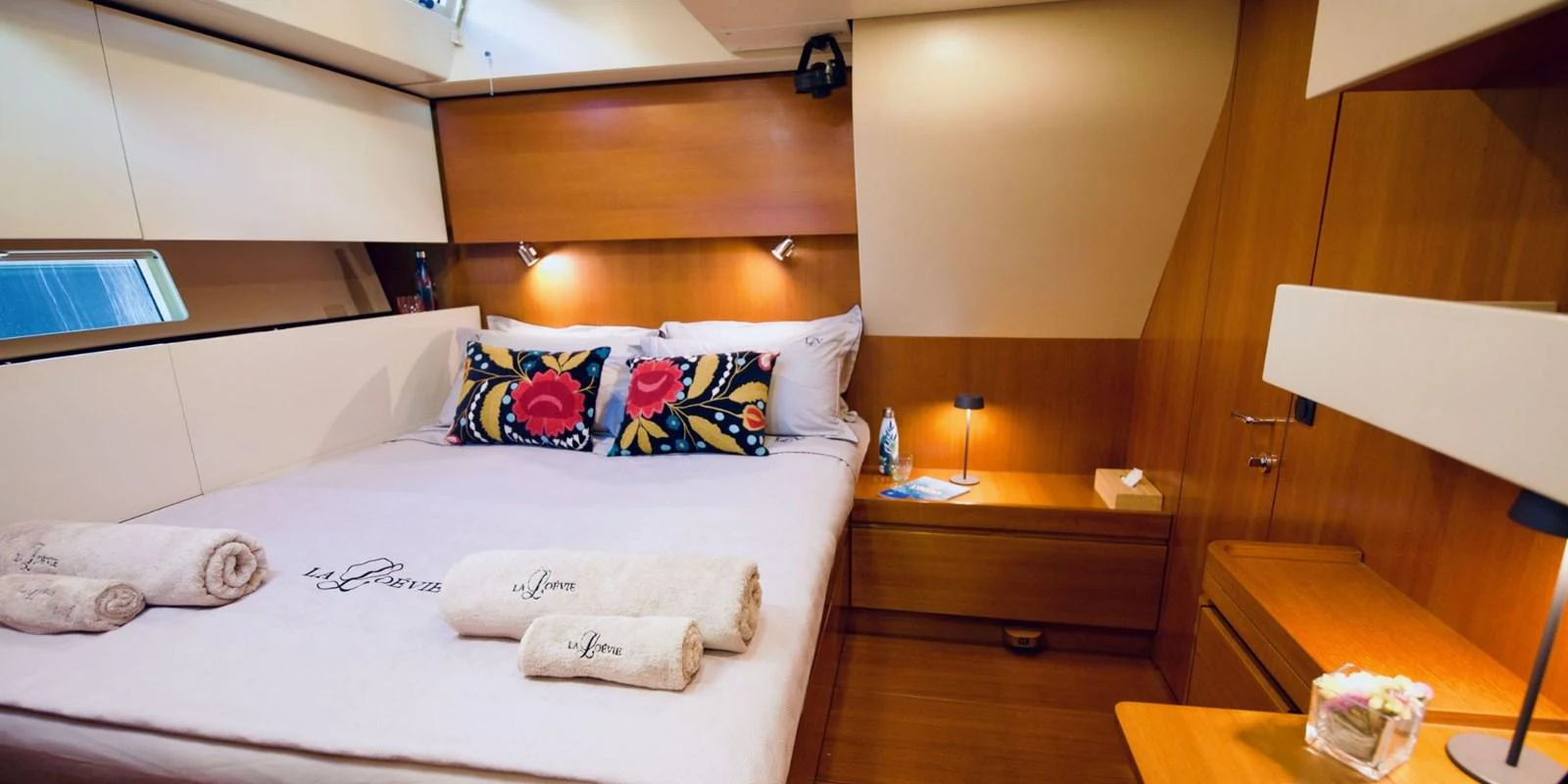 The stateroom features a cozy bed with vibrant pillows and warm wooden accents. aboard LA LOEVIE Yacht for Sale