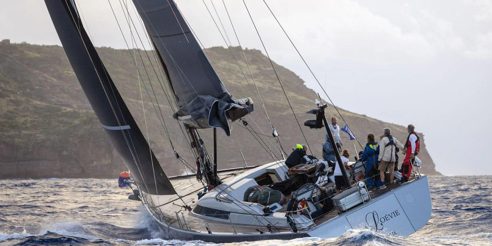 A sleek sailing yacht gracefully cuts through the water, heeling to starboard with a crew on deck. aboard LA LOEVIE Yacht for Sale