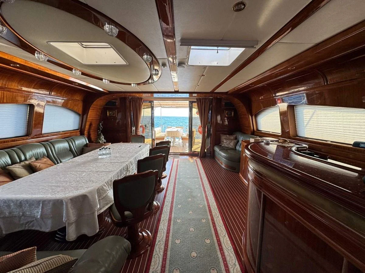 The yacht's salon features elegant wood paneling, a long dining table, and comfortable seating with a view of the aft deck. aboard PATRIOT Yacht for Sale