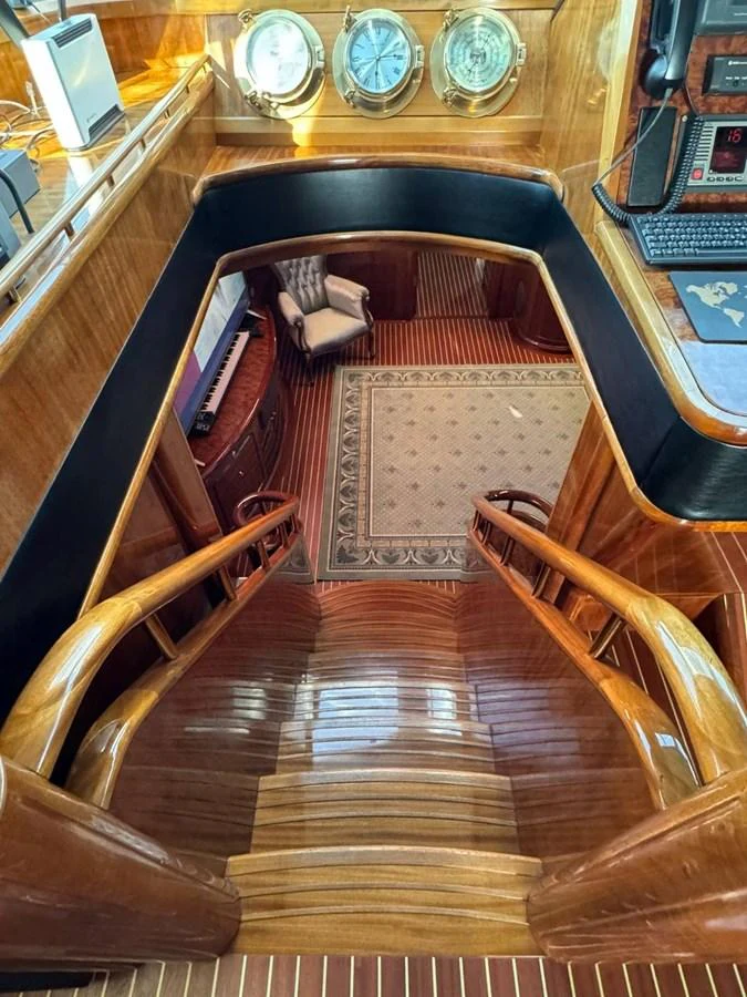 A luxurious wooden staircase leads down to a cozy seating area with nautical decor. aboard PATRIOT Yacht for Sale