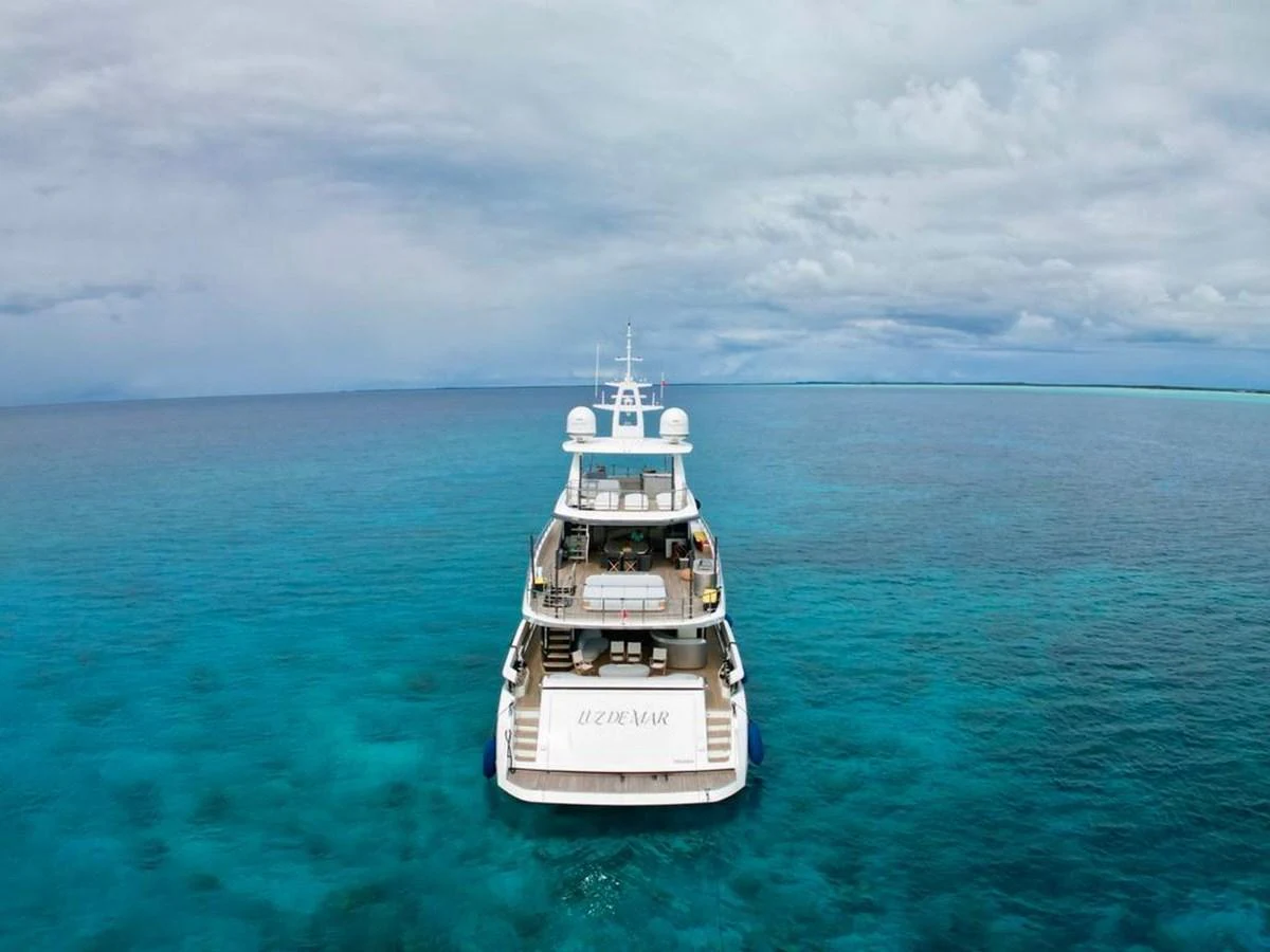 A luxurious yacht is anchored in crystal-clear turquoise waters under a vast, cloudy sky. aboard LUZ DE MAR Yacht for Sale