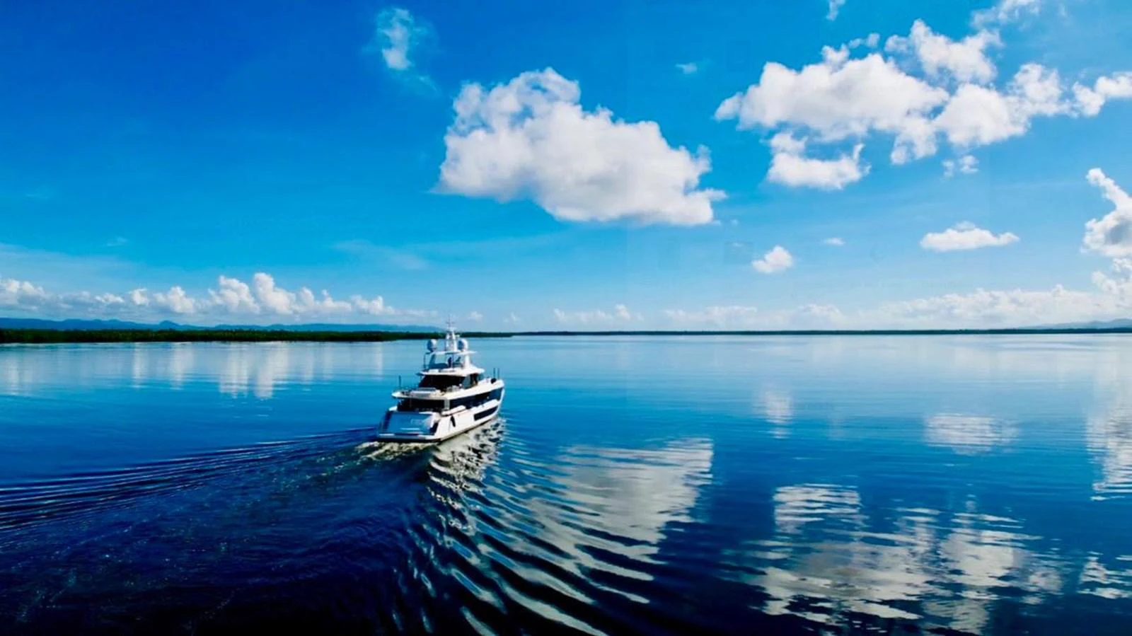 A stunning yacht cruises through calm, reflective waters under a bright blue sky. aboard LUZ DE MAR Yacht for Sale