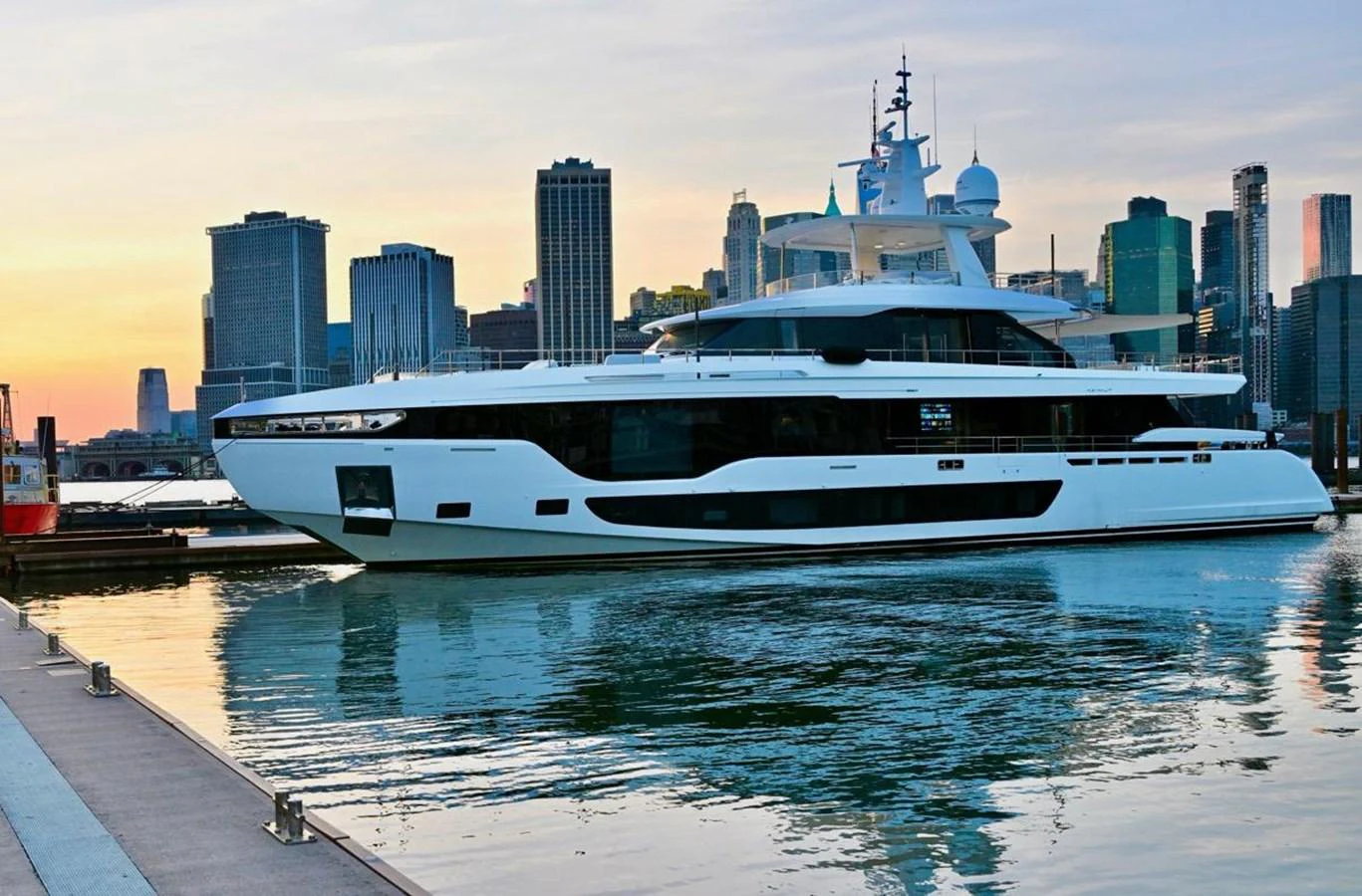 A sleek and modern yacht is docked in a vibrant city marina at sunset. aboard LUZ DE MAR Yacht for Sale