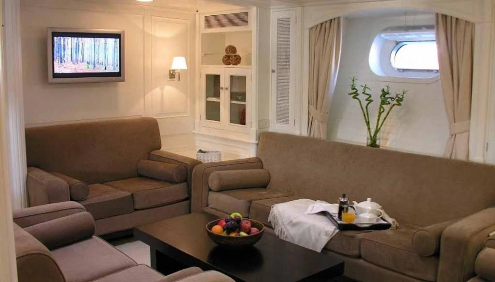 The salon features comfortable seating with a modern entertainment system and a view through a porthole. aboard MARI-CHA III Yacht for Sale